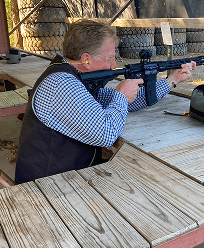 Kevin Hern shooting with a rifle at an outdoor range for a military or sports event.